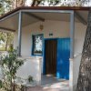 Bungalow bianco con porta blu, circondato da alberi e siepi.