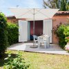 Patio esterno con tavolo e sedie bianche, ombrellone e giardino fiorito.