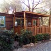 Esterno di una casa mobile in legno con terrazza coperta e giardino circostante.