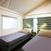 Due letti singoli in una tenda glamping con pareti chiare e testiera verde.