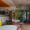 Interno di un bar con tavolini, sedie colorate, un bancone e frigoriferi per le bevande.