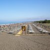 Ampia spiaggia con lettini e ombrelloni allineati, vista dell'oceano a sinistra.