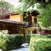 Edificio a due piani in legno e muratura con balcone, circondato da alberi e arbusti.