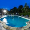 Piscina illuminata di notte con lettini blu e siepi intorno.