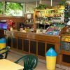 Interno di un bar con tavoli, sedie verdi e un bancone fornito di bevande e snack.