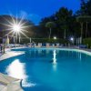 Una piscina illuminata di notte, circondata da lettini e alberi.