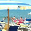 Spiaggia affollata, ombrelloni colorati, lettini e persone che si bagnano nel mare.