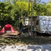 Un'area campeggio con roulotte, tenda rossa, sdraio e vegetazione circostante.
