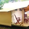 Una tenda con due sedie su una veranda in legno, circondata da alberi.