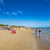 Una spiaggia affollata con persone che camminano lungo la riva sotto un cielo blu.