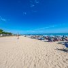 Spiaggia con sedie a sdraio, ombrelloni e campo da beach volley sotto un cielo sereno.