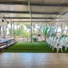 Sala con sedie bianche in plastica e un palco. Sullo sfondo, una pineta e spazi aperti.
