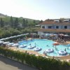 Una piscina circondata da lettini e ombrelloni, con un edificio e colline sullo sfondo.