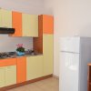 Cucina con mobili arancioni e gialli, un frigorifero e una piccola TV. Fiore in vaso sul piano.