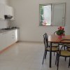 Cucina moderna bianca con tavolo da pranzo e sedie, pianta fiorita al centro del tavolo.