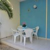 Tavolo bianco esterno con quattro sedie di plastica, parete blu e pianta verde.