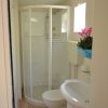 Un bagno con doccia ad angolo, lavabo e vaso. C'è una pianta fiorita accanto alla finestra.