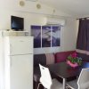 Sala da pranzo con tavolo scuro, sedie bianche, divano ad angolo e frigorifero con TV sopra.