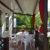Veranda con tavolo bianco e sedie, circondata da piante e tendine rosse.