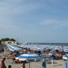 Spiaggia con ombrelloni blu e bianchi, molte persone presenti.