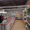 Interno di un supermercato con scaffali pieni di prodotti e un banco frigo.