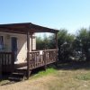 Un bungalow con veranda in legno, circondato da arbusti sotto un cielo sereno.