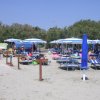 Spiaggia con ombrelloni blu e lettini, frequentata da bagnanti sotto il sole.