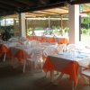 Terrazza esterna di un ristorante con tavoli apparecchiati e tovaglie arancioni.