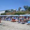 Spiaggia affollata con ombrelloni blu e persone sdraiate su lettini.