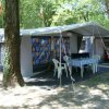 Una tenda campeggio con tavolo e sedie bianche sotto un baldacchino, circondata da alberi.