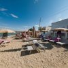 Spiaggia con lettini, ombrelloni beige e persone che prendono il sole vicino al mare.