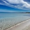 Spiaggia con sabbia chiara, mare cristallino e cielo azzurro parzialmente nuvoloso.