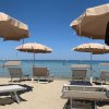 Ombrelloni beige e lettini su una spiaggia sabbiosa con mare calmo sullo sfondo.