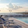 Piscina sul tetto con lettini blu e vista panoramica sul mare al tramonto.