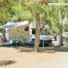 Un camper parcheggiato con sedie e tavolo sotto un telone, circondato da alberi.