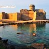 Un castello sul mare al tramonto, circondato da acqua cristallina.