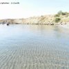 Spiaggia deserta con acqua limpida e colline erbose sullo sfondo.