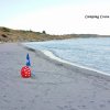 Spiaggia sabbiosa con ombrelloni e pallone rosso. Campeggio Costa Splendente sullo sfondo.