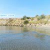 Spiaggia con acqua calma, colline erbose e un cartello di campeggio in lontananza.