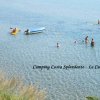Persone nuotano in un mare limpido, vicino a un kayak e una tavola da surf.