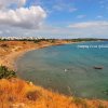 Vista panoramica di una spiaggia con scogliere, vegetazione e case bianche in lontananza.