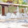 Bungalow bianco con piante fiorite e porta in legno, circondato da alberi.