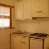 Cucina compatta con mobili bianchi, lavello, piano cottura e finestra con tende.
