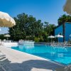 Piscina all'aperto con ombrelloni e lettini bianchi, circondata da alberi e un edificio blu.