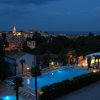 Vista notturna di una piscina illuminata e una città sullo sfondo.