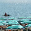 Spiaggia con ombrelloni verdi e bianchi, barca a remi in mare.