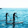 Due persone fanno paddleboarding su un mare calmo sotto un cielo luminoso.