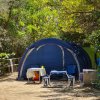 Tenda blu con tavolo e sedie all'aperto, circondata da alberi verdi.
