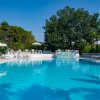 Una piscina con lettini e ombrelloni, circondata da alberi verdi.