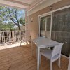 Veranda in legno con tavolo bianco, sedie e vista su alberi.